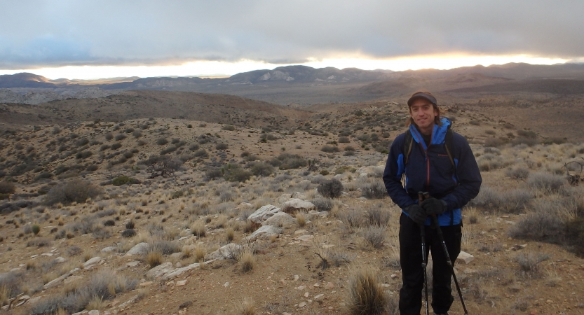 A person wearing hiking gear smiles for a photo while standing in a desert landscape